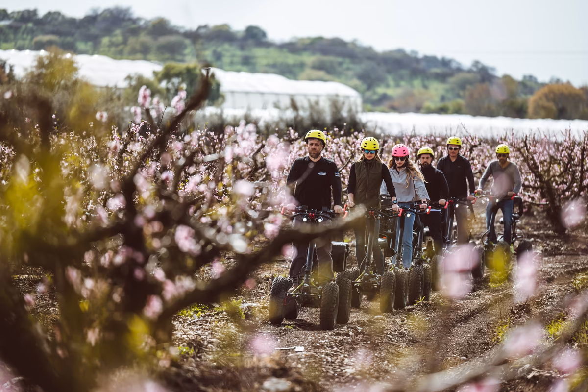 A group of helmeted EZ Raider riders on a path through a flowering orchard
